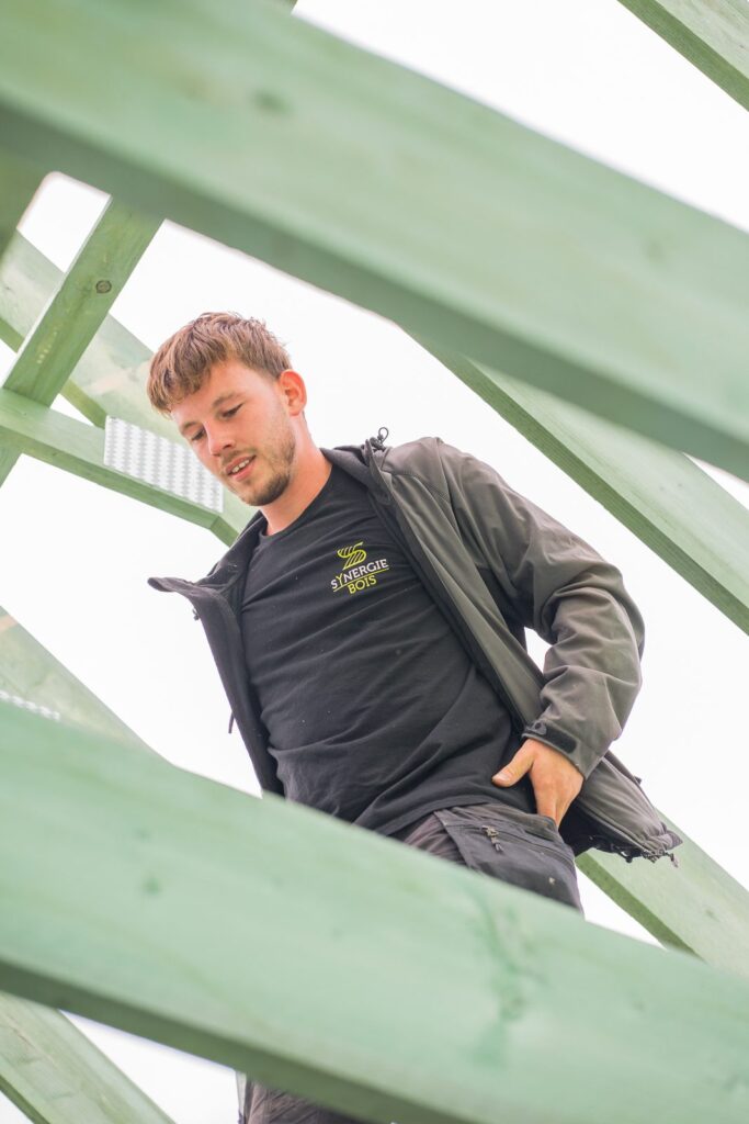 Membre de l'équipe Synergie Bois au milieu d'une charpente en bois